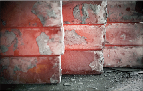 Close-up of stacked red bricks with spalled and peeling surfaces.